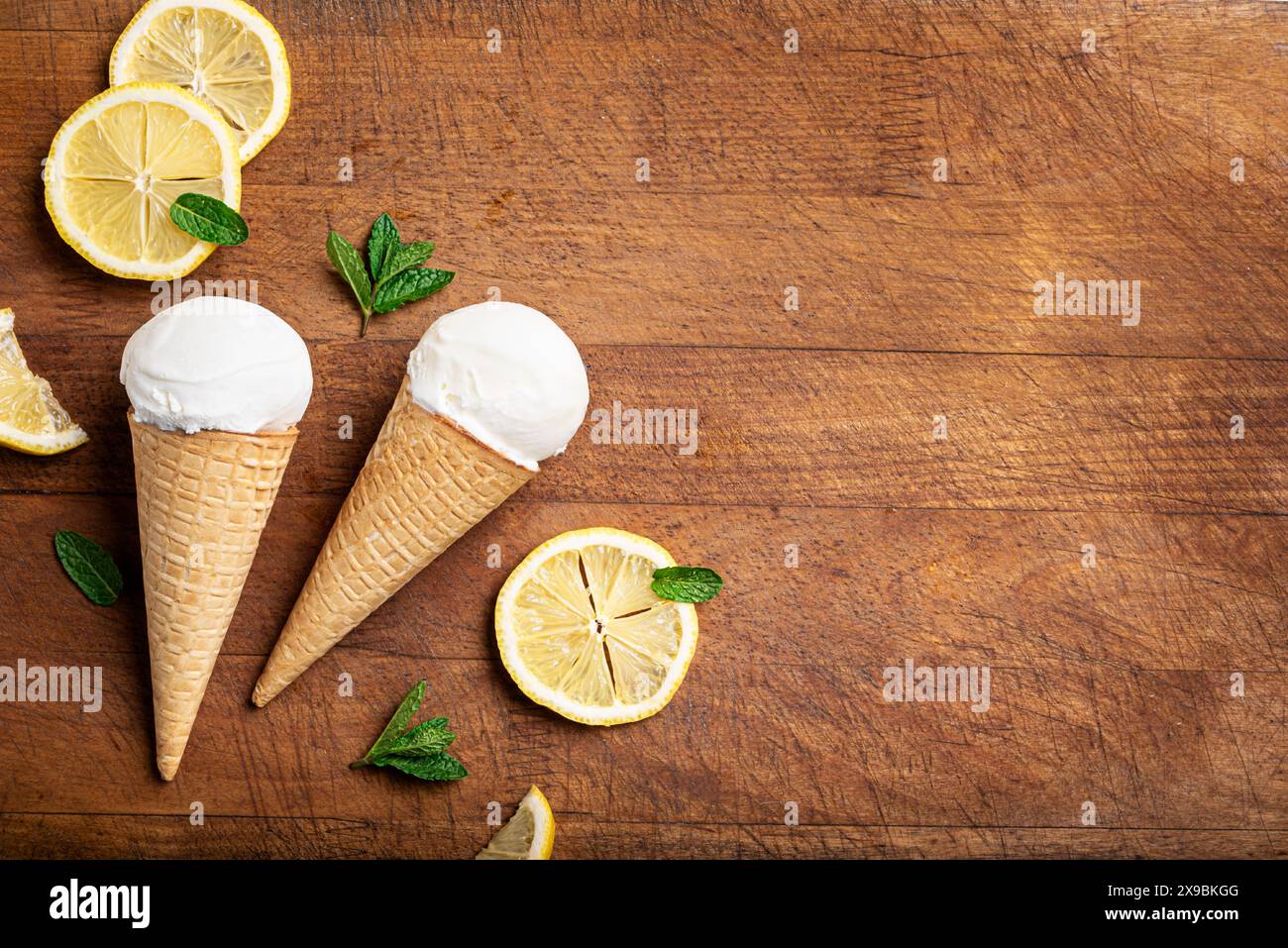 Cuillère de crème glacée au citron dans un cône de gaufre et tranches de citron sur fond de bois, vue de dessus, espace de copie. Crème glacée végétalienne au citron et à la noix de coco maison. Banque D'Images