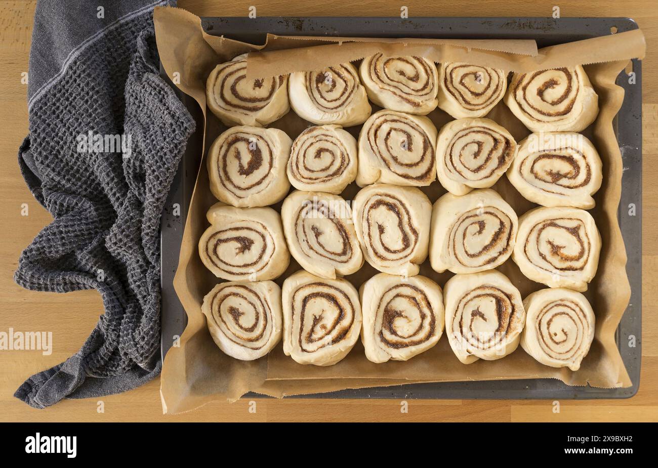Photographie alimentaire de table de petits pains à la cannelle prêts à cuire dans une plaque de cuisson avec une table en bois de hêtre en papier cuisson Banque D'Images