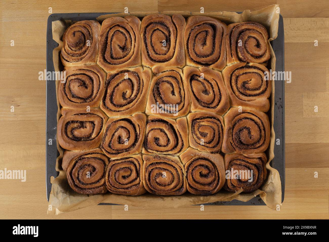 Photographie de nourriture de table de petits pains à la cannelle cuits dans un plateau de cuisson avec papier cuisson table en bois de hêtre Banque D'Images