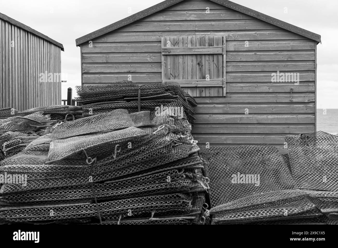 Tapis d'huîtres et cages empilés devant un hangar en bois à Whitstable Harbour, Kent, tons et textures noir et blanc Banque D'Images