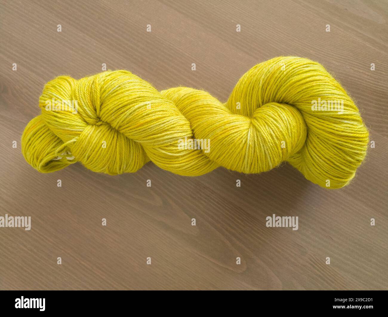 Photo de dessus de table d'un écheveau de fil mince tordu jaune-vert teint à la main sur un fond en bois Banque D'Images