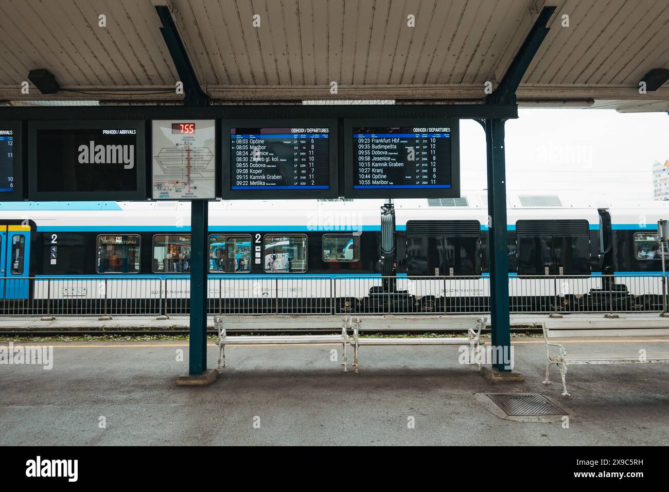 Un train régional des chemins de fer slovènes tourne au ralenti sur une voie ferrée à la gare de Ljubljana, en Slovénie. Un écran de télévision affiche les arrivées et les départs Banque D'Images