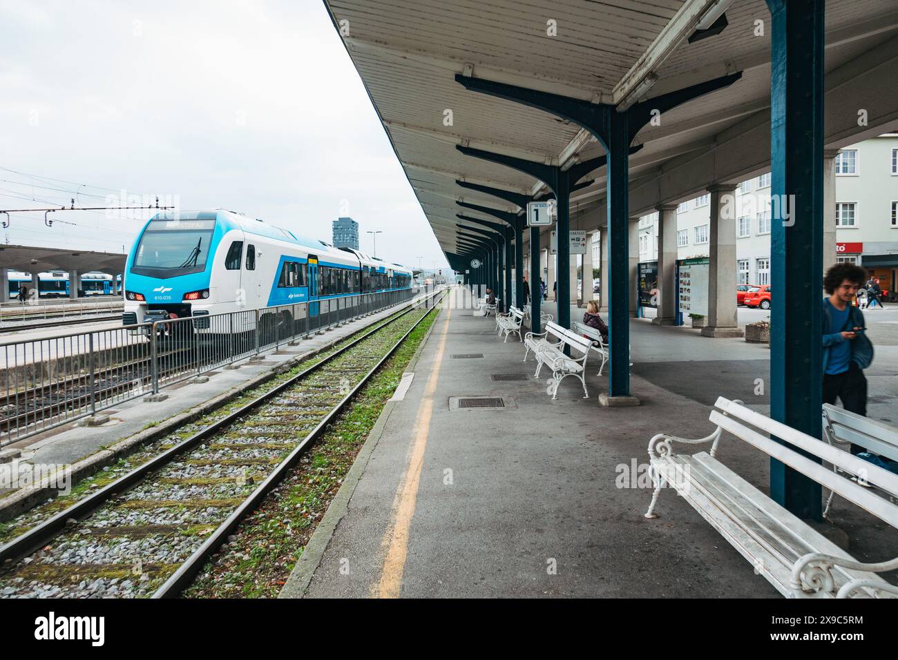 Un train bleu et blanc des chemins de fer slovènes régionaux tourne au ralenti sur une piste à la gare de Ljubljana, en Slovénie. Un abri pend au-dessus de la plate-forme Banque D'Images