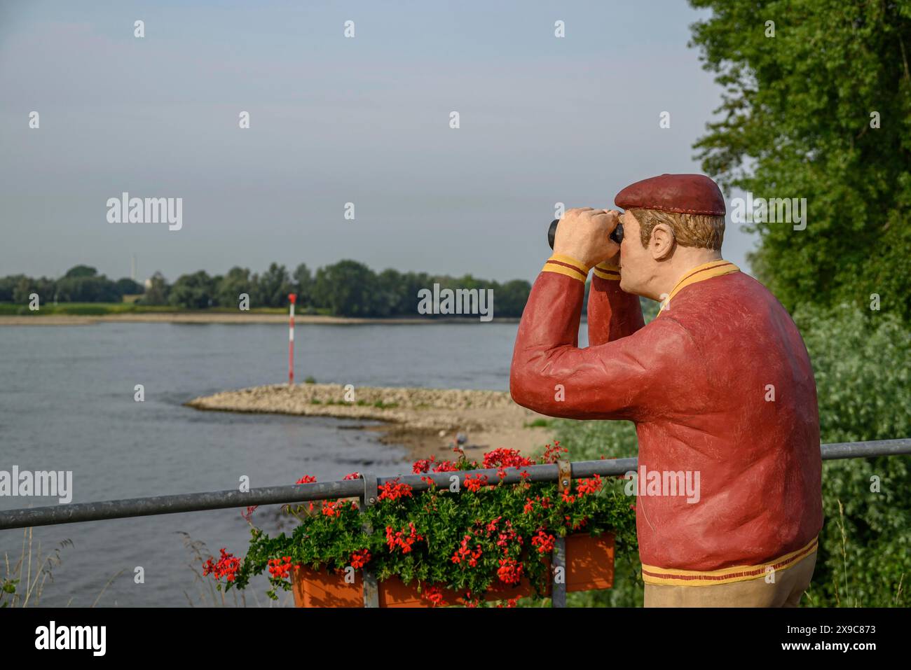 Statue d'homme avec des jumelles au bord de la rivière, fleurs au premier plan et arbres en arrière-plan, la promenade rhénane de Rees avec des fleurs et Banque D'Images