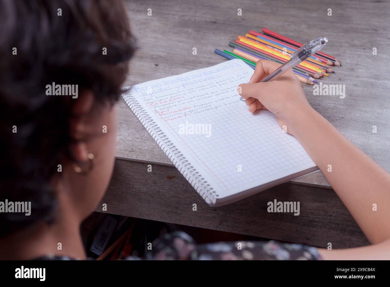 Gros plan des mains d'une jeune femme faisant ses devoirs, elle écrit dans son cahier, sujet des devoirs. Banque D'Images