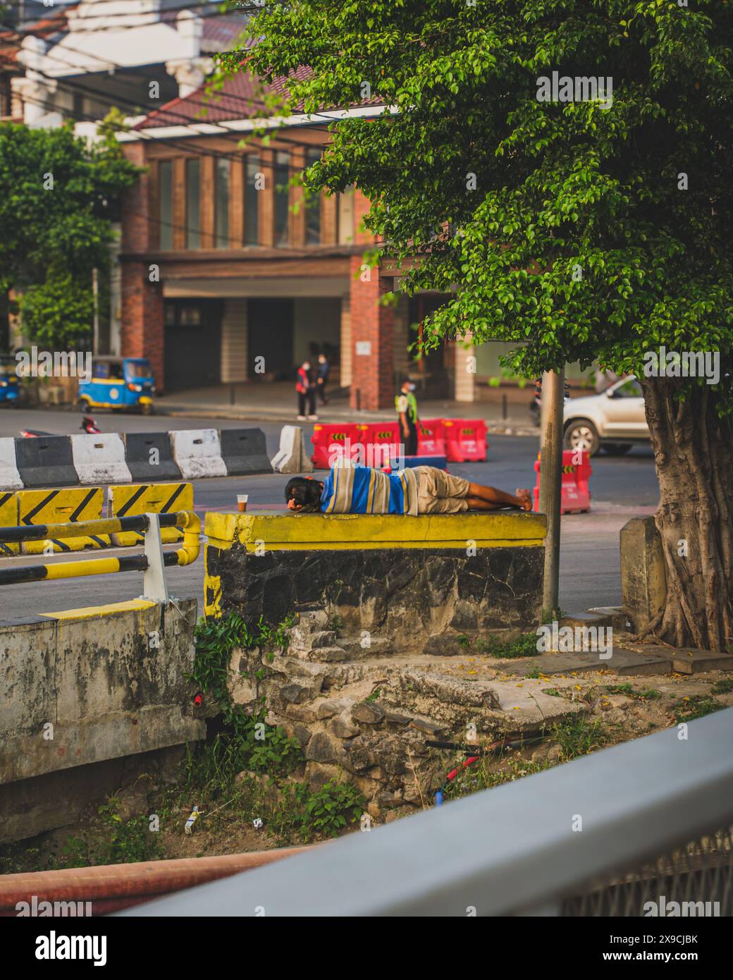 Jakarta, Indonésie - 7 mai 2024. Un sans-abri dort près de la rue, il y a une tasse de café à proximité. Banque D'Images