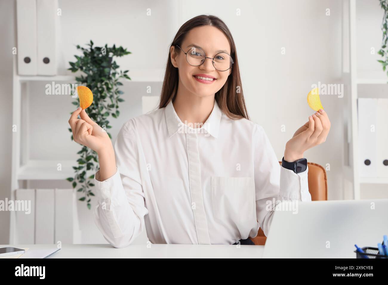 Jeune femme d'affaires avec des chips de pomme de terre au bureau Banque D'Images