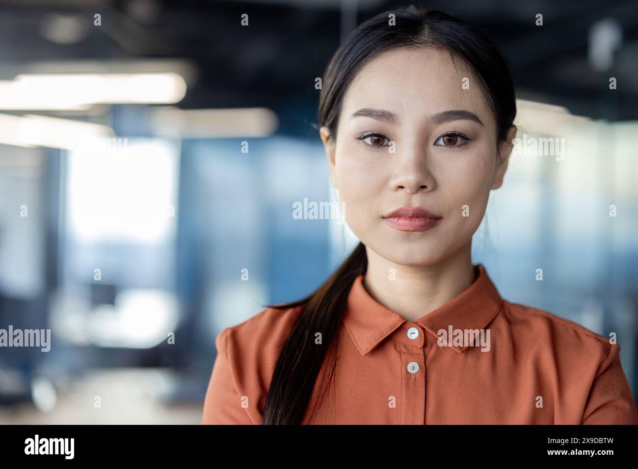 Gros plan portrait d'une femme d'affaires asiatique sérieuse confiante sur le lieu de travail à l'intérieur du bureau regardant soigneusement à la caméra, employé de bureau féminin près de la fenêtre. Banque D'Images