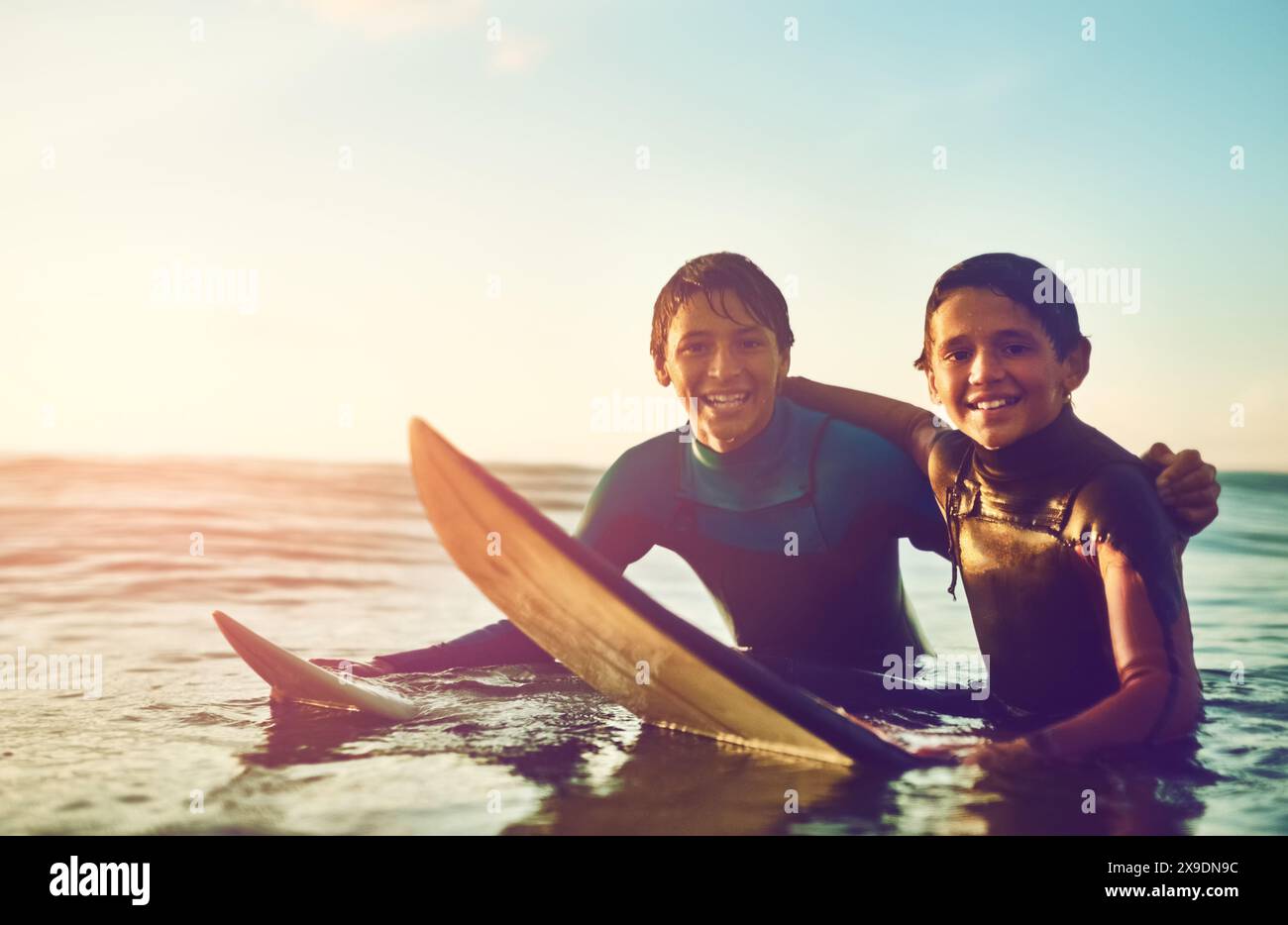 Enfants, portrait et heureux dans l'eau pour le surf, le sport et le bien-être avec planche, ciel bleu et sourire. Excité, les garçons et la natation à la plage comme surfeur pour Banque D'Images