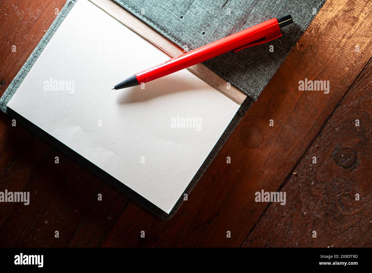 Un cahier ouvert avec des pages vierges et un stylo rouge posé dessus, placé sur une surface en bois. Banque D'Images