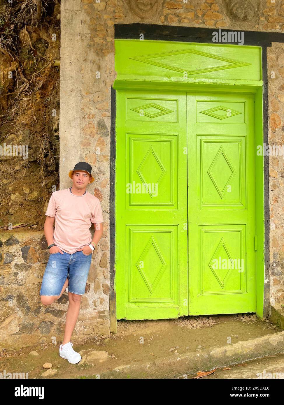 Homme décontracté s'appuyant contre une porte verte vibrante sertie dans un mur de pierre, dégageant une ambiance détendue et élégante. Banque D'Images