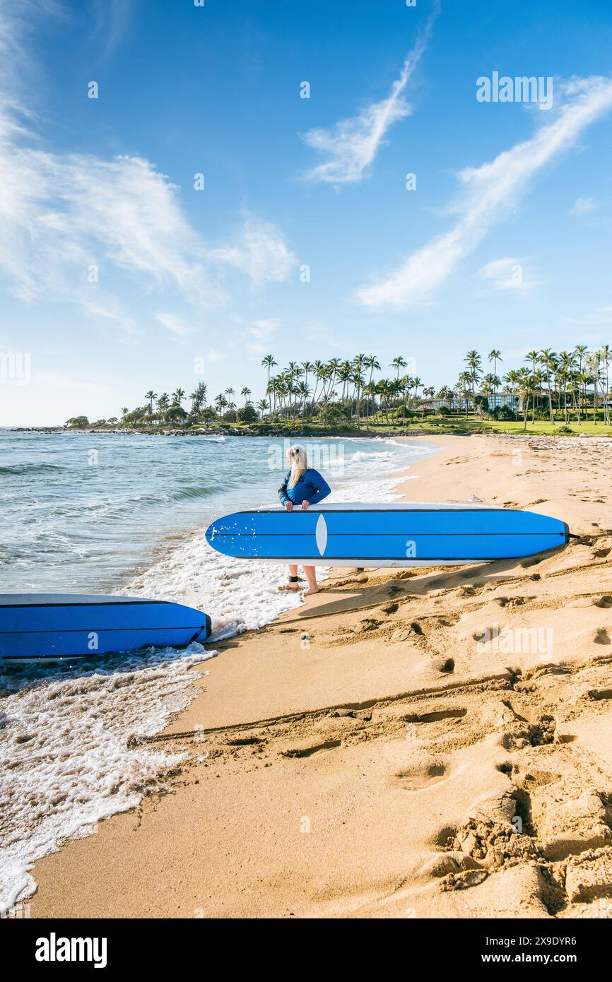Une femme aux longs cheveux blonds porte sa longue planche dans l'OCE Banque D'Images