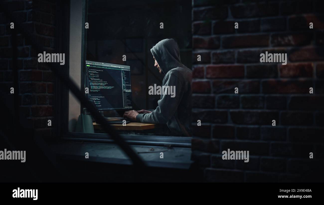 Appartement de nuit : Hacker masculin maléfique portant un sweat à capuche pénètre dans la salle du serveur de données, attaque DDOS, programme de phishing, malware. Darknet Cyber crime concept. Vue de l'extérieur dans la fenêtre. Banque D'Images