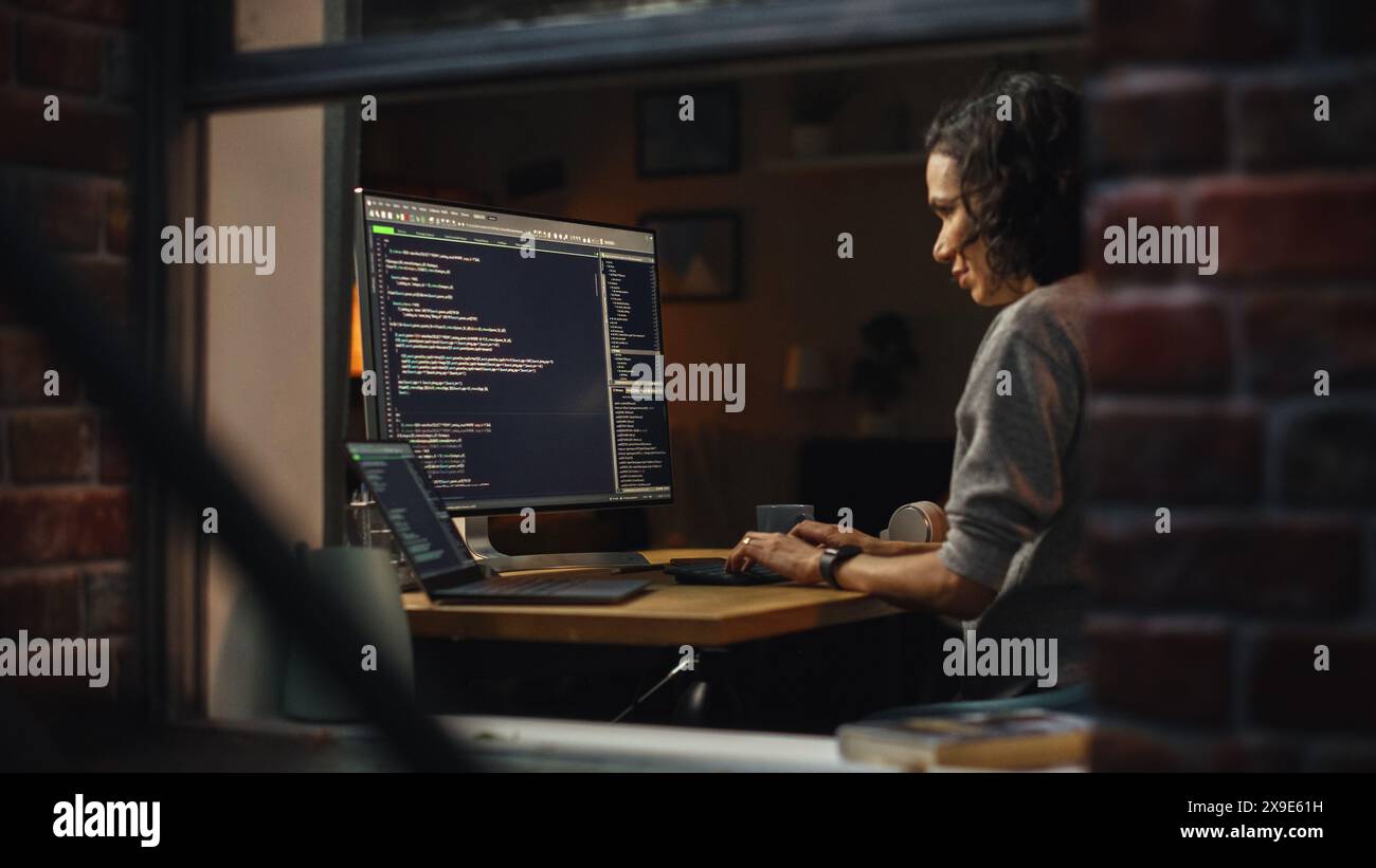 Bureau à domicile de nuit : jeune femme hispanique travaille sur ordinateur de bureau. Développeur de logiciels, entrepreneur de commerce électronique écriture Code pour l'application e-Business, Programme de conception. Vue de l'extérieur dans la fenêtre. Banque D'Images