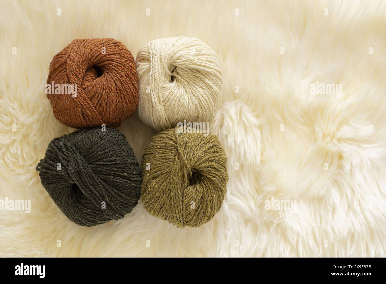 Photographie vue de dessus de quatre écheveaux de fil de laine de tweed sur fond de fourrure d'agneau blanche à la lumière naturelle Banque D'Images