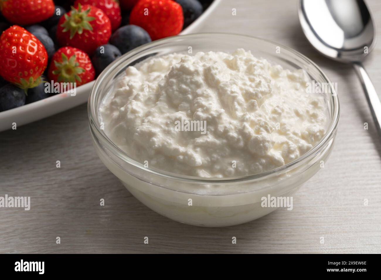 Bol en verre avec du fromage cottage en gros plan et des fruits frais en arrière-plan Banque D'Images
