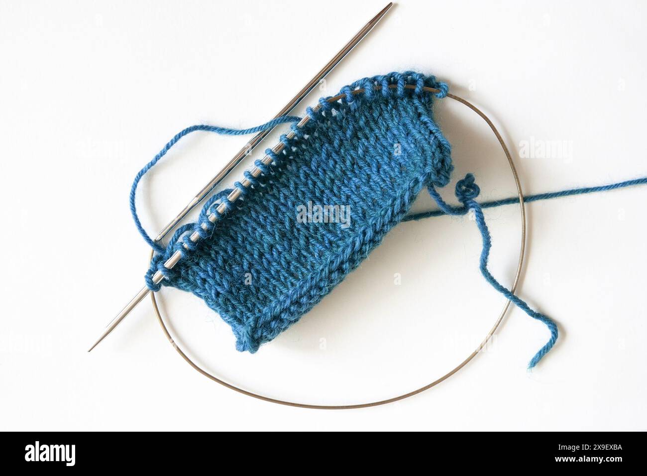 Photographie de table du projet de tricot bleu turquoise Stockinette Stitch sur aiguilles circulaires sur fond blanc Banque D'Images
