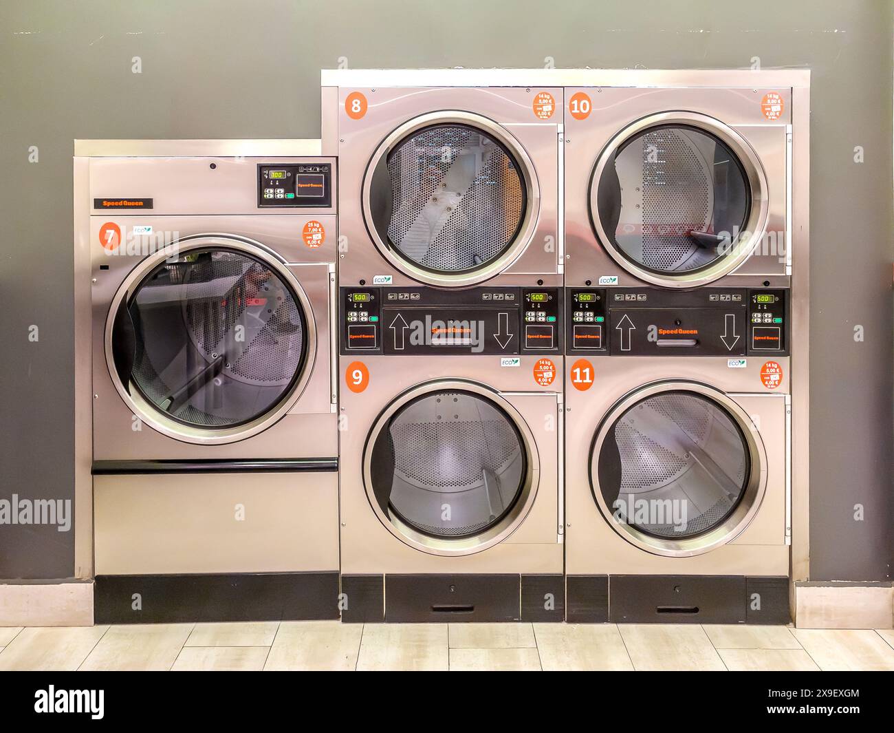 Sèche-linge industriel avec panneaux de commande numériques dans une laverie automatique en libre-service, aligné et numéroté. Banque D'Images