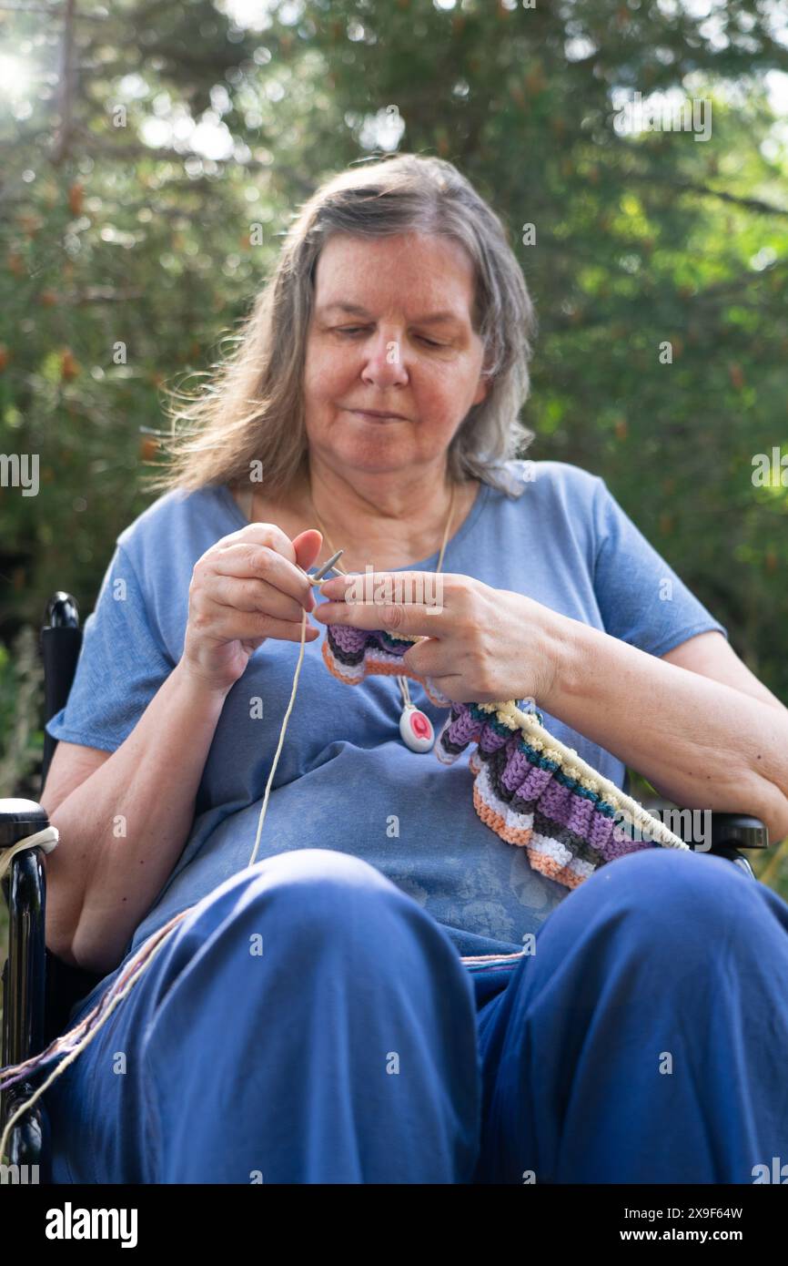 Femme de plus de 60 ans en fauteuil roulant tricotant à l'extérieur Banque D'Images