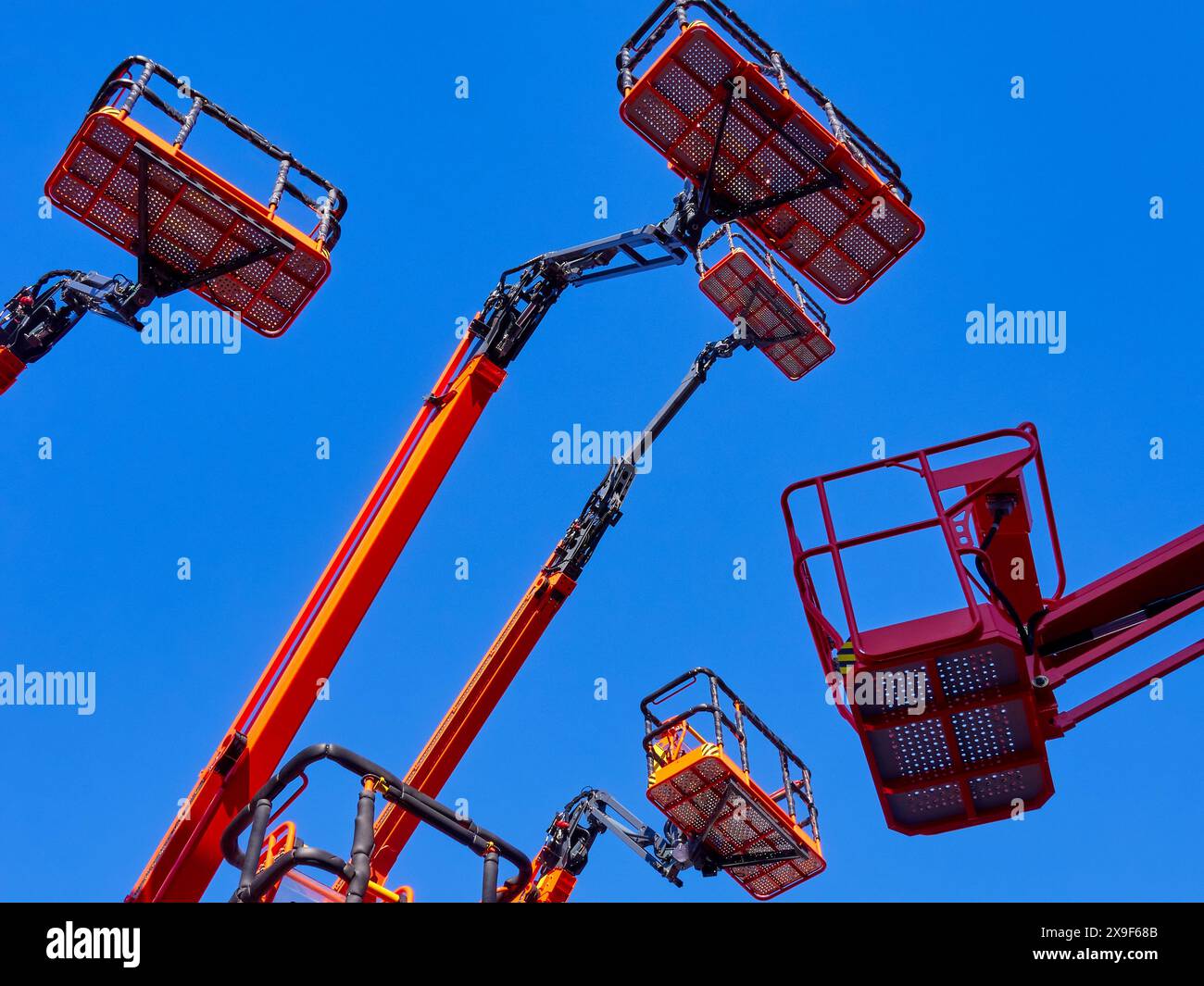 Grand groupe de grues articulées, paniers et bras hydrauliques haut dans un ciel bleu clair, plan de perspective à faible angle. Banque D'Images