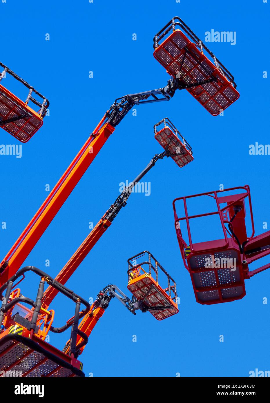 Grand groupe de grues articulées, paniers et bras hydrauliques haut dans un ciel bleu clair, plan de perspective à faible angle. Banque D'Images