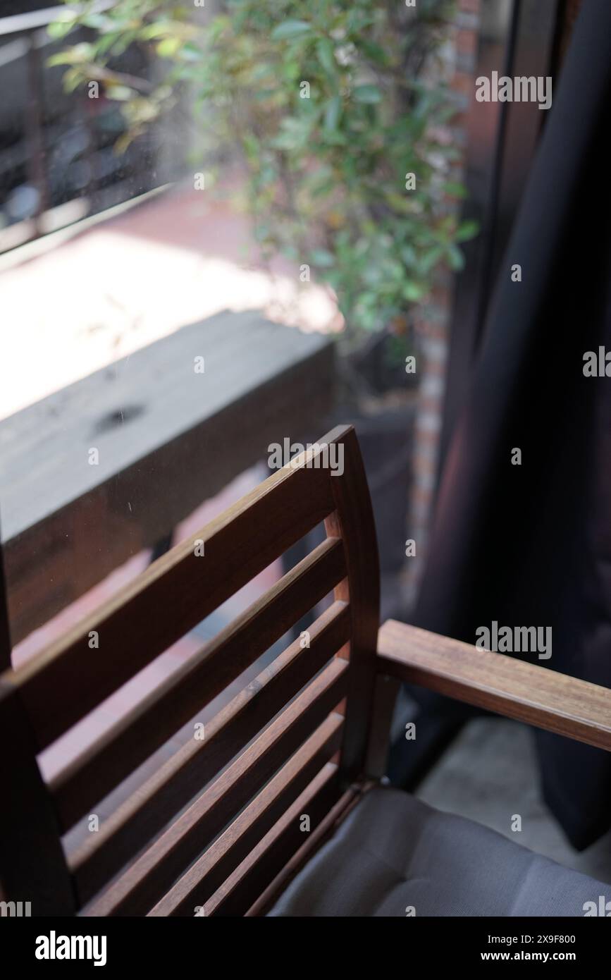 Vue instantanée esthétique et minimale de balcon rideau de chaise en bois plante verte par le mur de verre. Banque D'Images