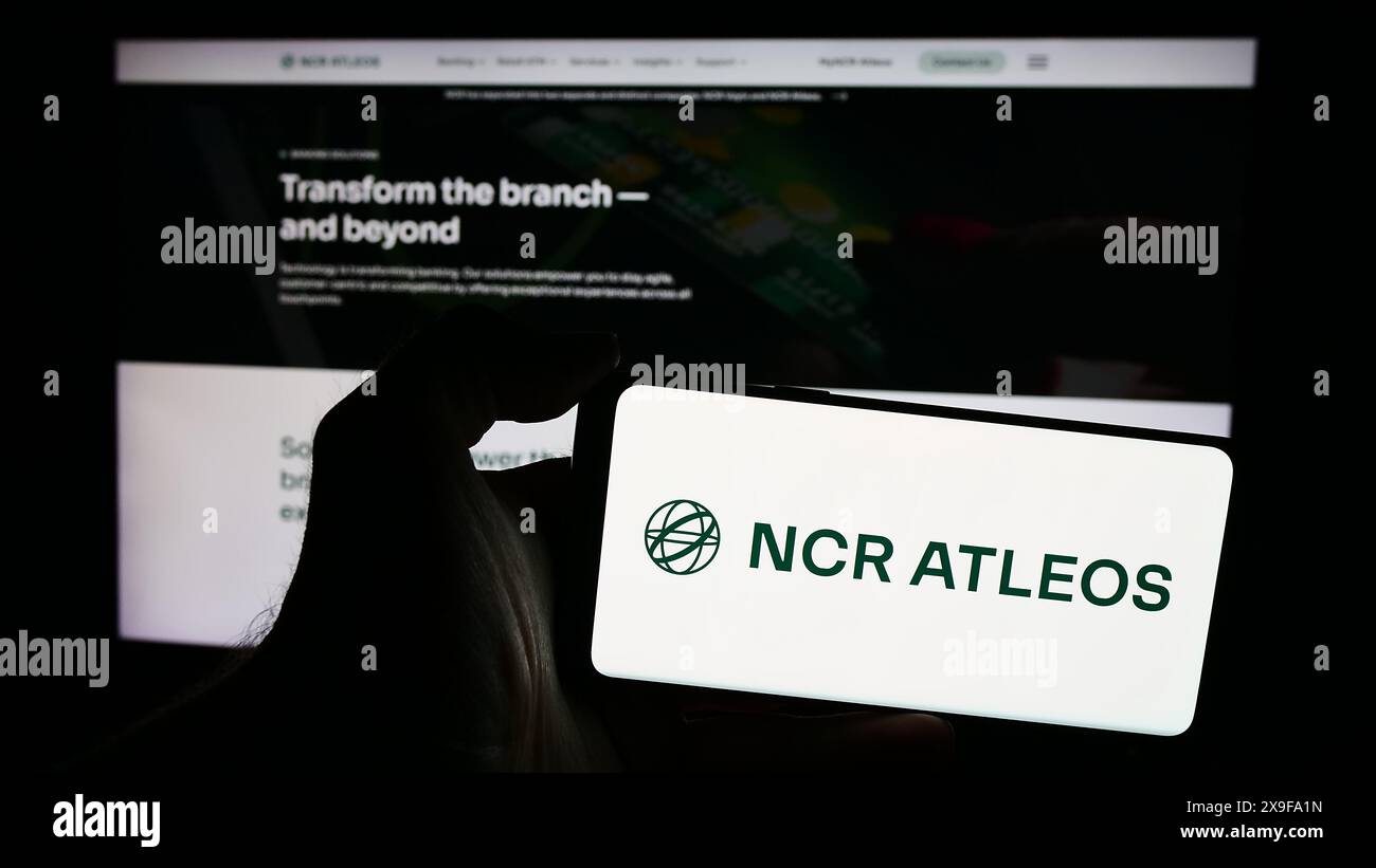 Personne tenant un smartphone avec le logo de la société de services financiers américaine NCR Atleos Corporation en face du site Web. Concentrez-vous sur l'affichage du téléphone. Banque D'Images