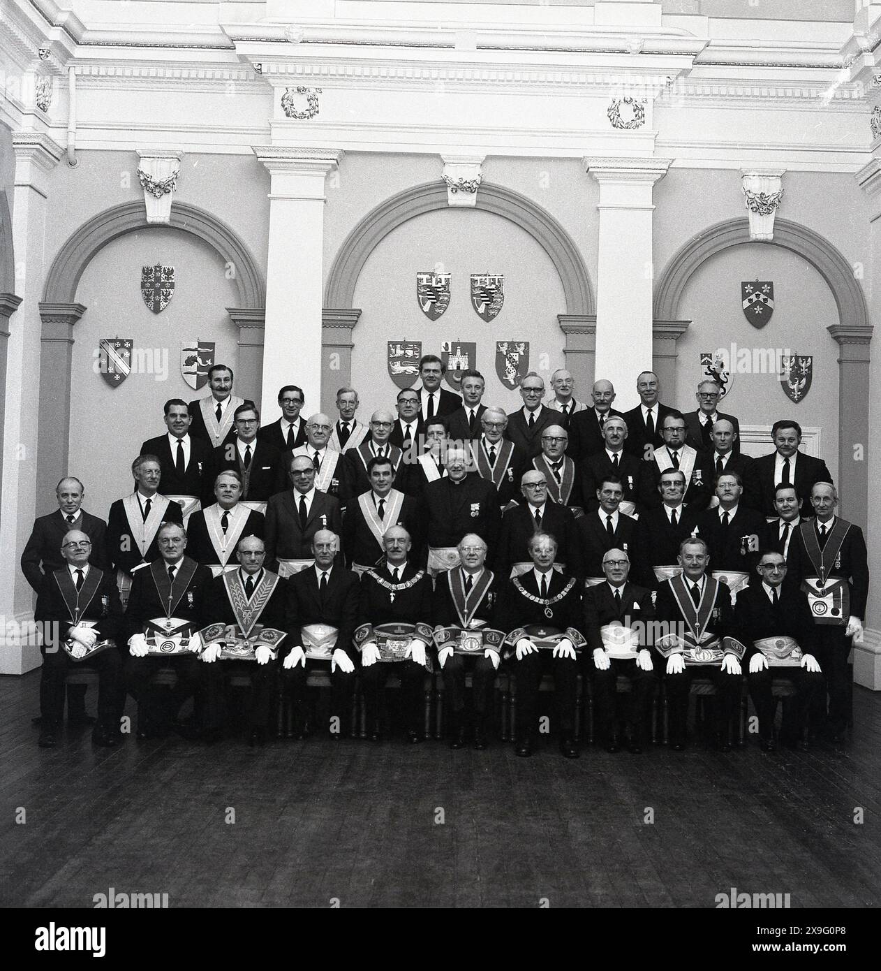 Années 1960, historique, groupe de maçons ou de francs-maçons en robes réunis pour une photo à l'intérieur du hall d'une loge maçonnique, Angleterre, Royaume-Uni. Datant de centaines d'années aux guildes locales de tailleurs de pierre, la fraternité maçonnique est une société fraternelle où les membres jurent de se soutenir mutuellement et de garder ce soutien secret, à moins qu'ils n'aient enfreint la loi. Banque D'Images