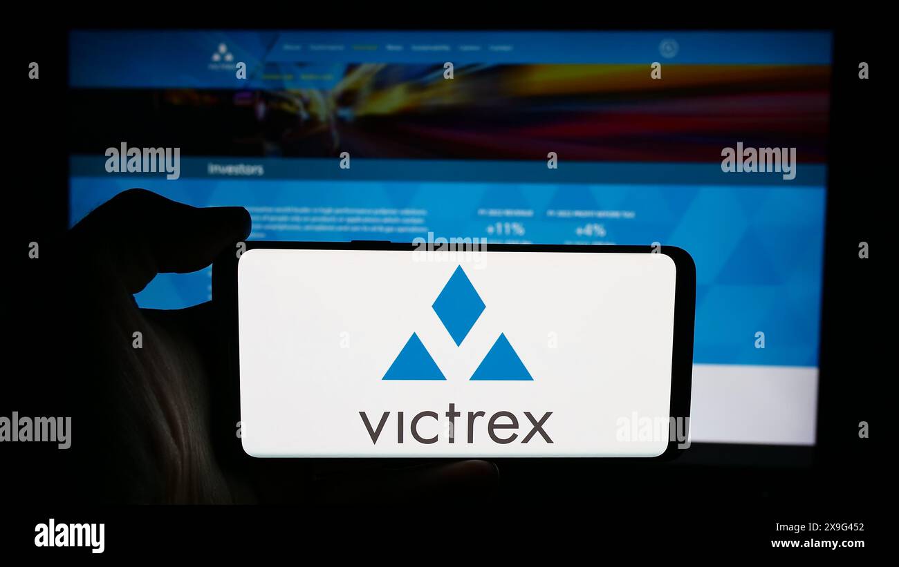 Personne tenant le téléphone portable avec le logo de la société britannique de production de polymère Victrex plc en face de la page Web de l'entreprise. Concentrez-vous sur l'affichage du téléphone. Banque D'Images