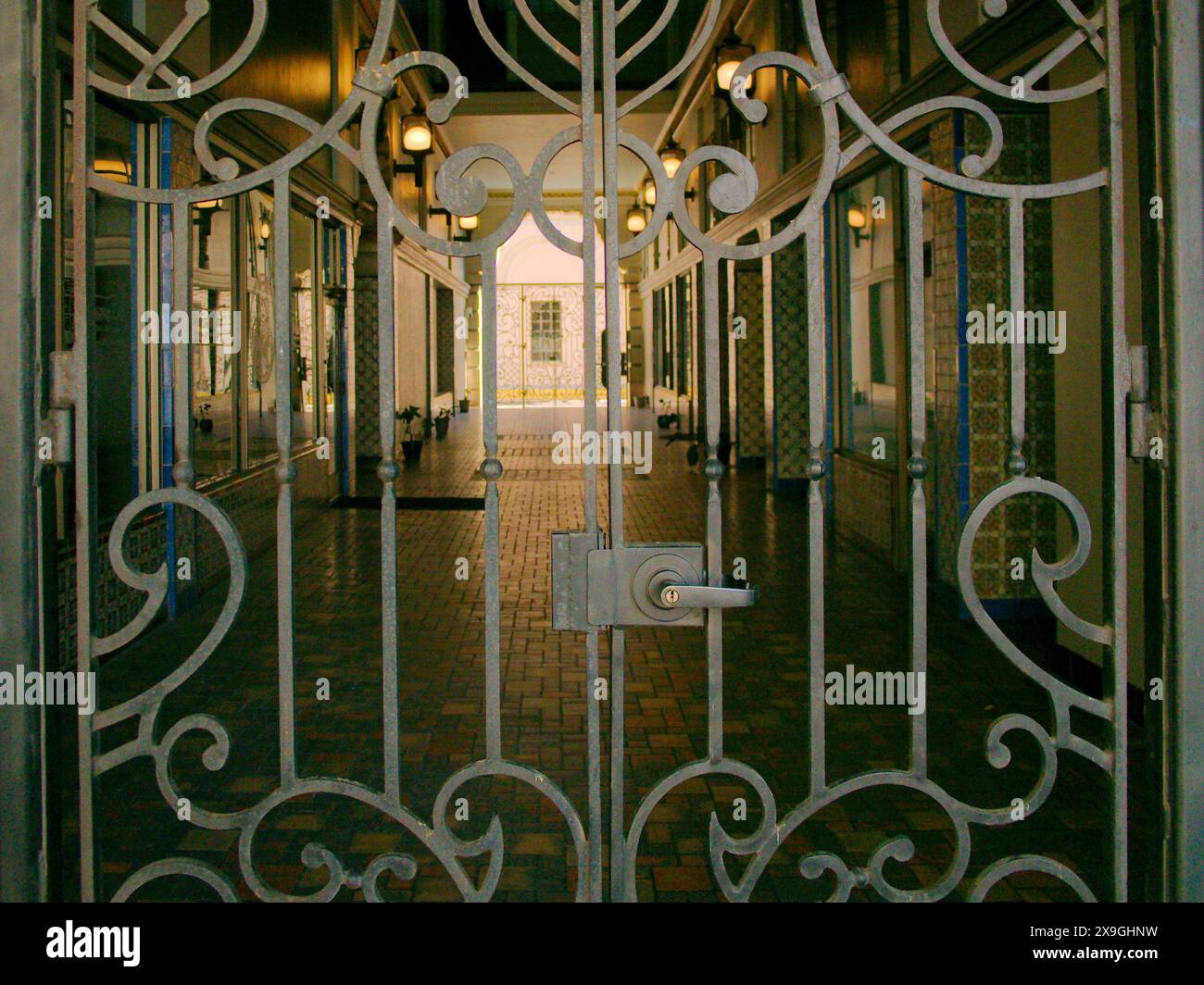 Vue à travers la porte en métal d'acier à l'ancienne passerelle d'arcade avec carrelage au sol avec soleil et ombre. L'ouverture latérale éloignée conduit à une lumière vive. Banque D'Images