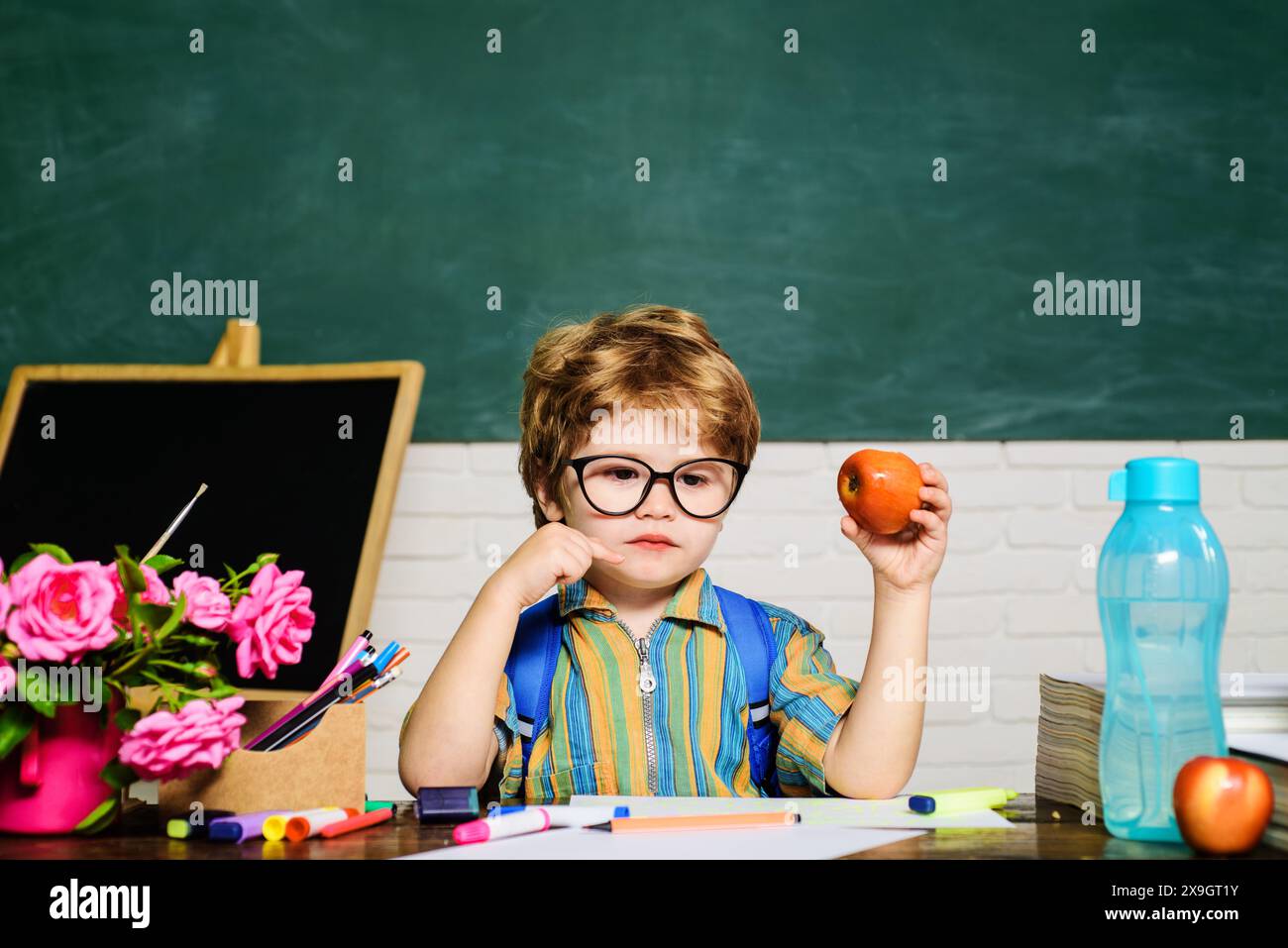 Déjeuner scolaire pendant la pause. Petit garçon étudiant déjeunant avec une pomme en classe. Élève de l'école primaire assis à table mangeant pomme à Banque D'Images