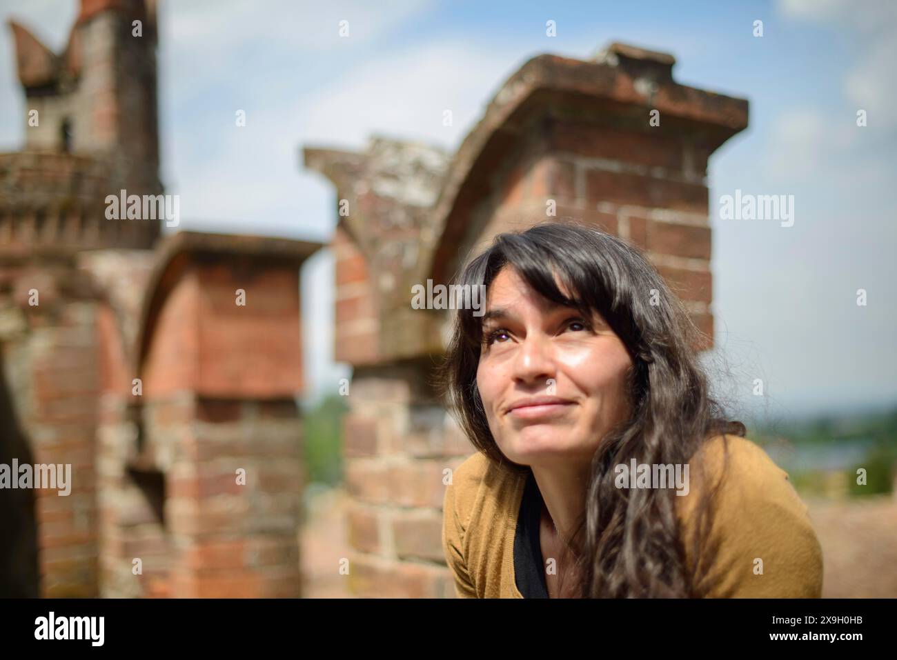 Réfléchie jeune femme latino est assise sur un vieux mur de briques, habillée de façon décontractée, profitant d'un moment paisible dans un cadre extérieur rustique Banque D'Images