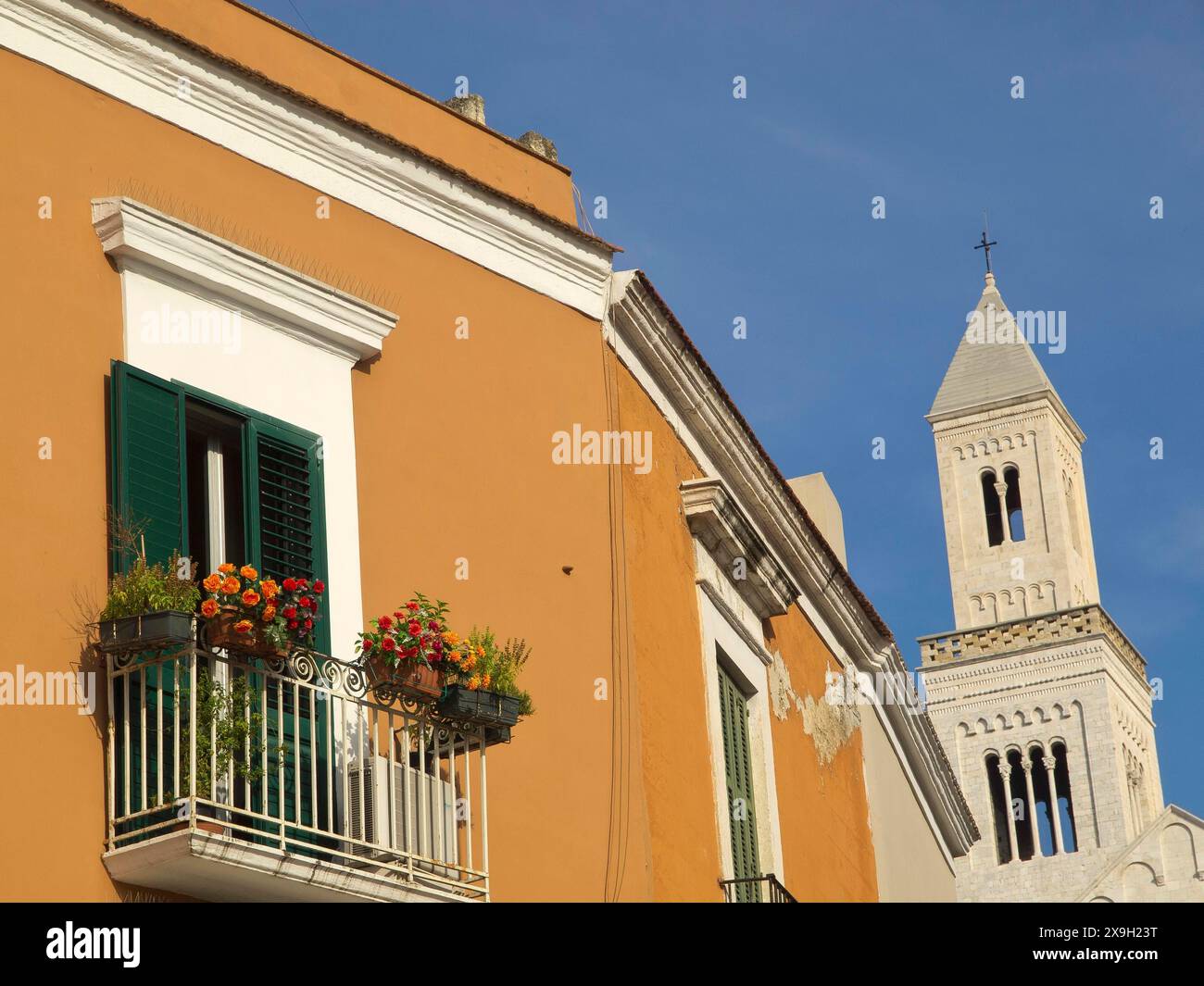 Façade colorée avec volets verts, balcon avec fleurs et une tour d'église contre un ciel bleu clair, la ville de Bari sur la Méditerranée avec Banque D'Images