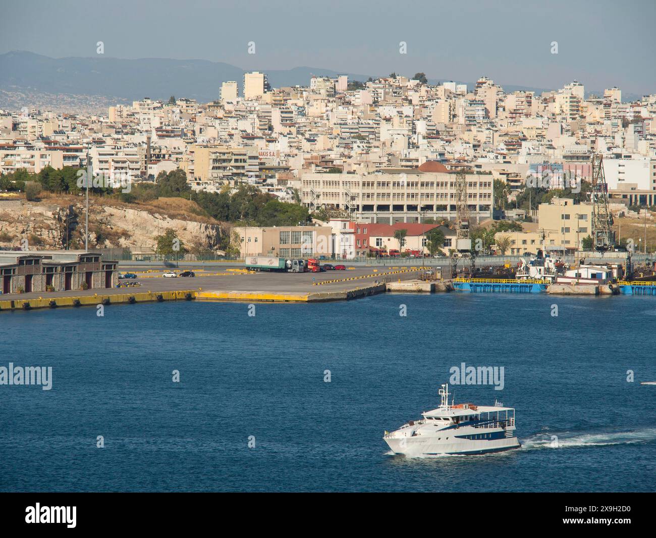 Un bateau navigue dans le port, en arrière-plan de nombreux bâtiments de la ville, bâtiments anciens avec des colonnes et des arbres sur l'Acropole à Athènes Banque D'Images