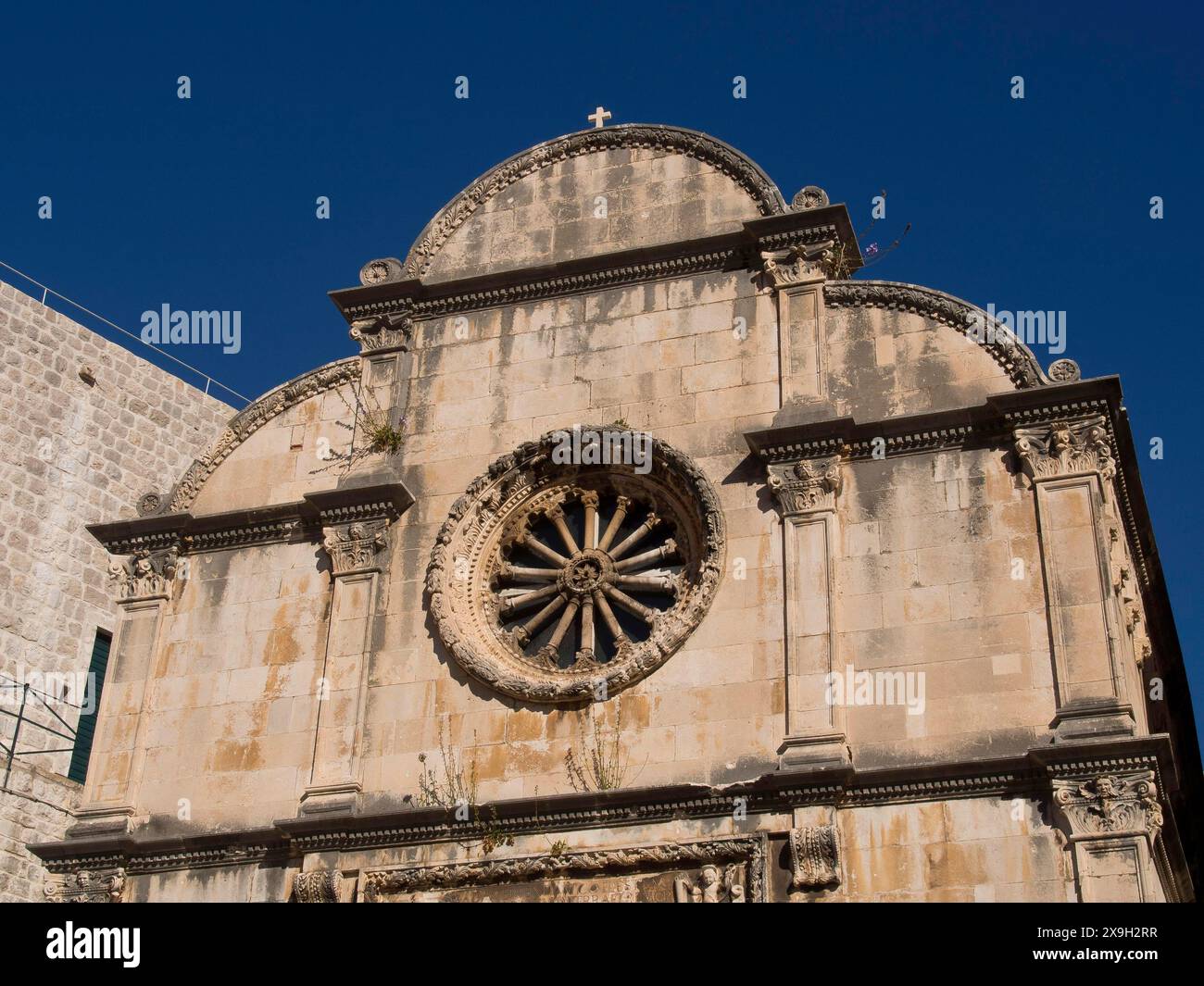 Une vieille église avec une façade en pierre détaillée et une rosace sous un ciel bleu clair, la vieille ville de Dubrovnik avec des maisons historiques, des églises, rouge Banque D'Images
