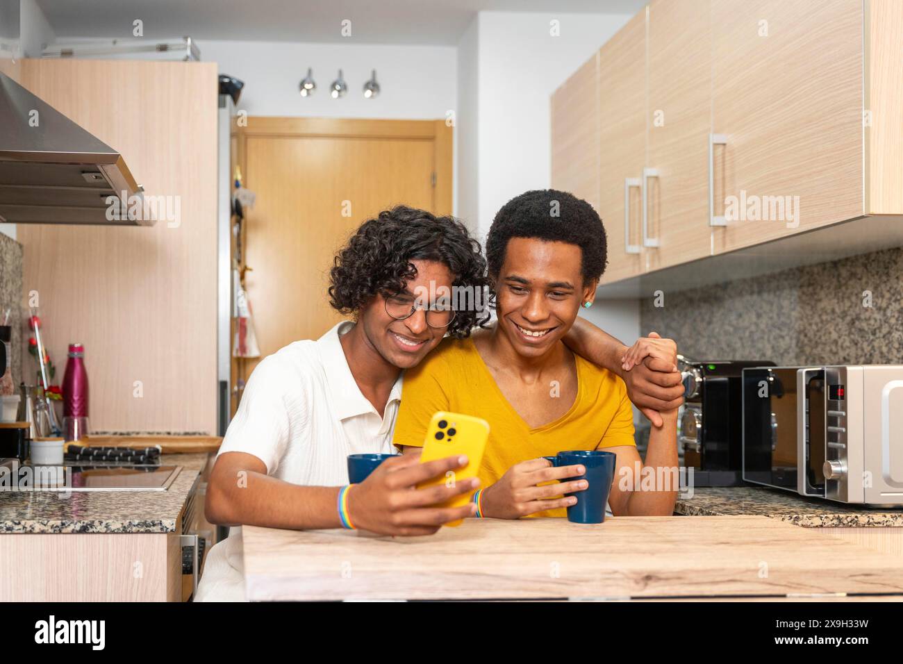 Couple adulte latin gay partageant un téléphone mobile tout en buvant un café du matin à la maison Banque D'Images