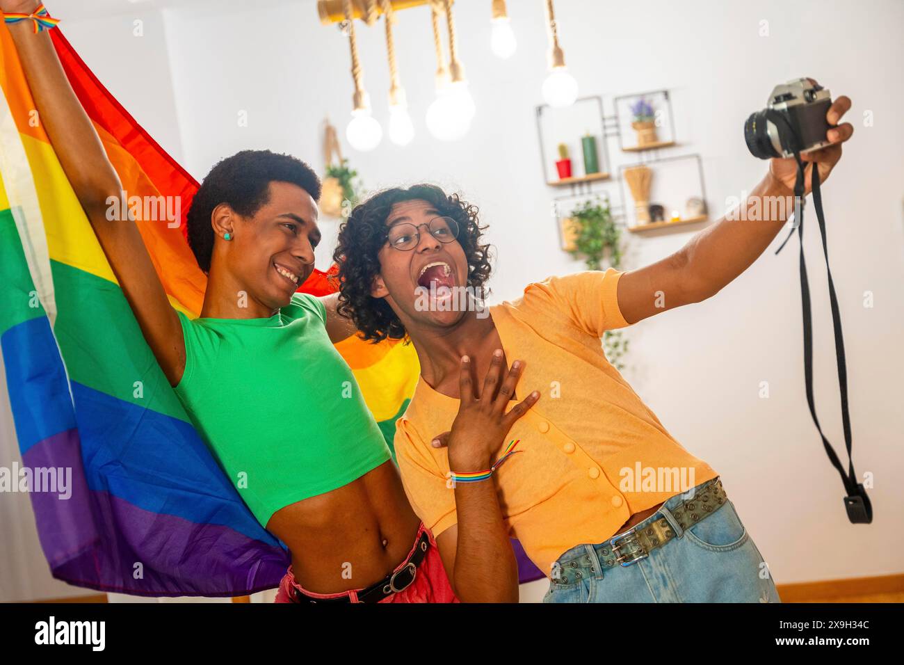 Jeune couple gay latin prenant un selfie avec un appareil photo tout en élevant le drapeau lgbt arc-en-ciel à la maison Banque D'Images