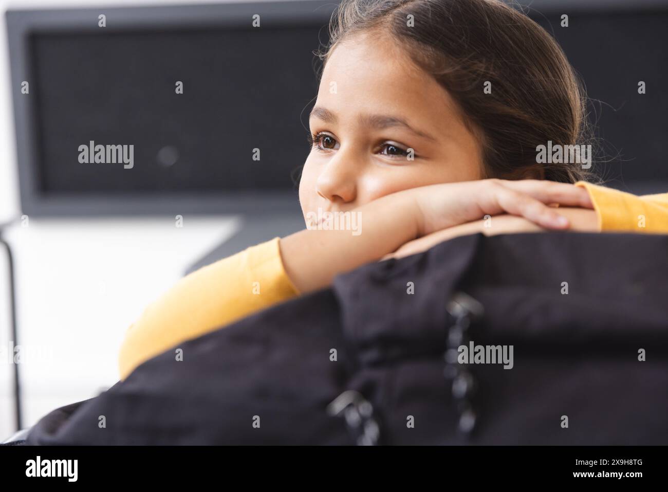 À l'école, jeune étudiante biraciale se reposant le menton sur les mains, regardant loin dans la salle de classe Banque D'Images