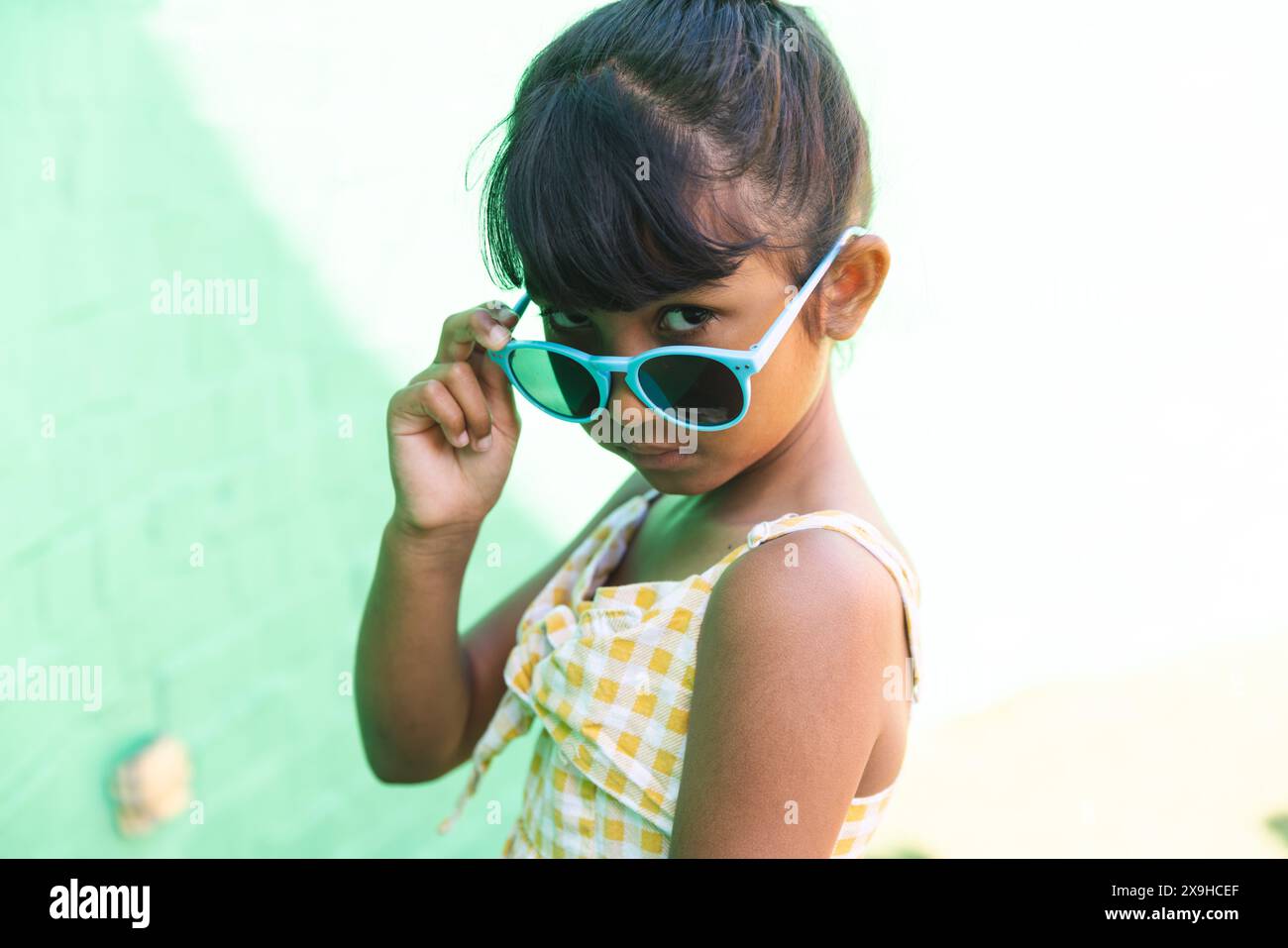 Fille biraciale portant des lunettes de soleil et une robe de soleil pose ludique à l'extérieur Banque D'Images