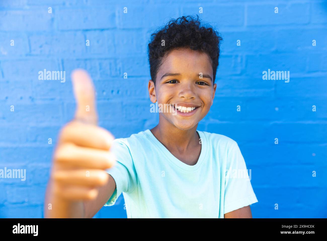 Biracial Boy donne un pouce contre un mur bleu Banque D'Images
