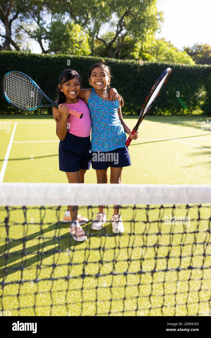 À l'extérieur, deux jeunes sœurs biraciales souriant sur un court de tennis, tenant des raquettes de tennis Banque D'Images