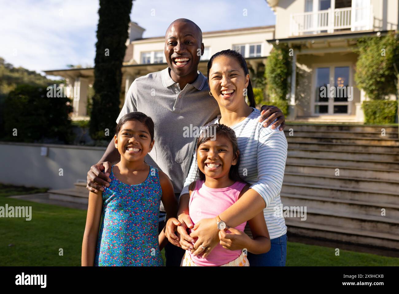 En plein air, heureuse famille biraciale de quatre souriants ensemble devant leur maison Banque D'Images