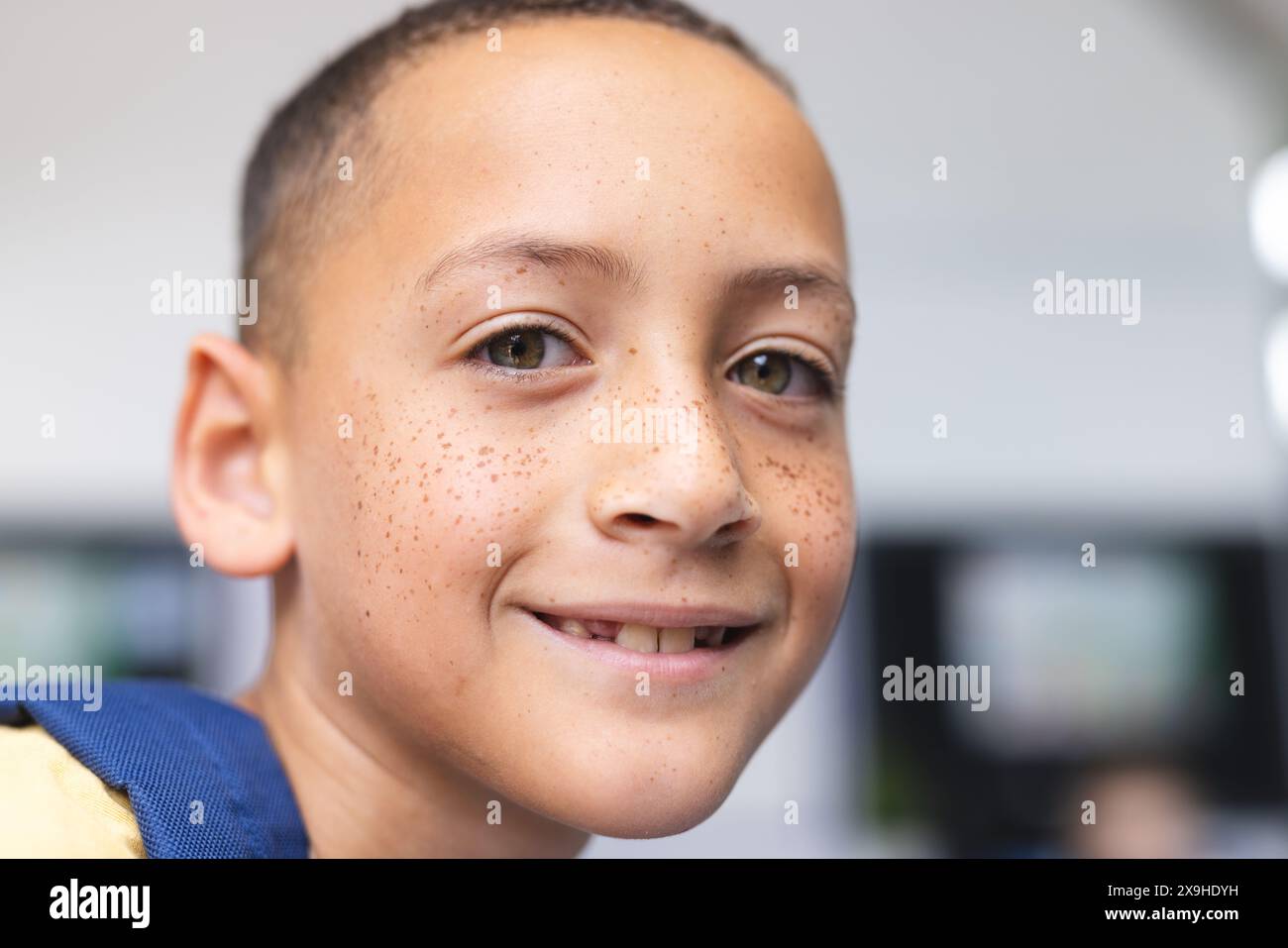 Garçon biracial avec des taches de rousseur sourit chaleureusement dans une salle de classe d'école, ses yeux bruns brillants Banque D'Images