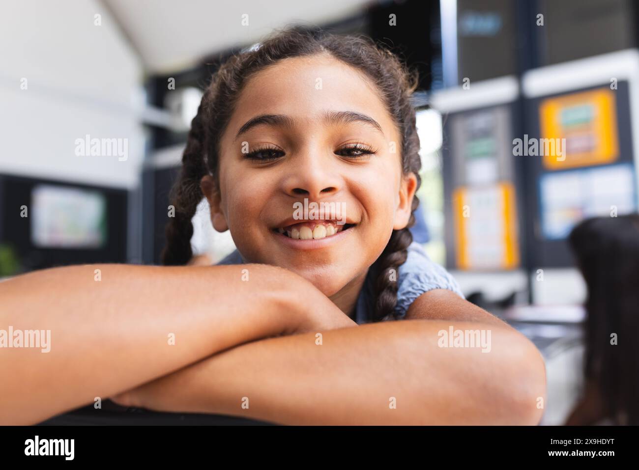 Une fille biraciale aux cheveux tressés sourit chaudement, reposant son menton sur ses bras Banque D'Images