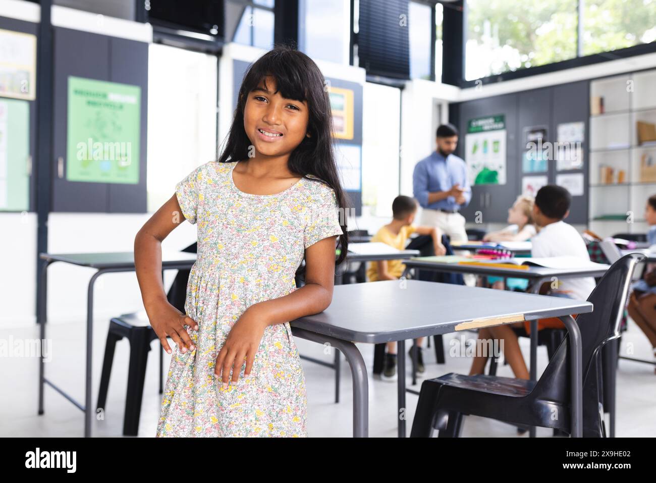 Fille biraciale avec de longs cheveux foncés se tient avec confiance dans une salle de classe d'école avec espace de copie Banque D'Images