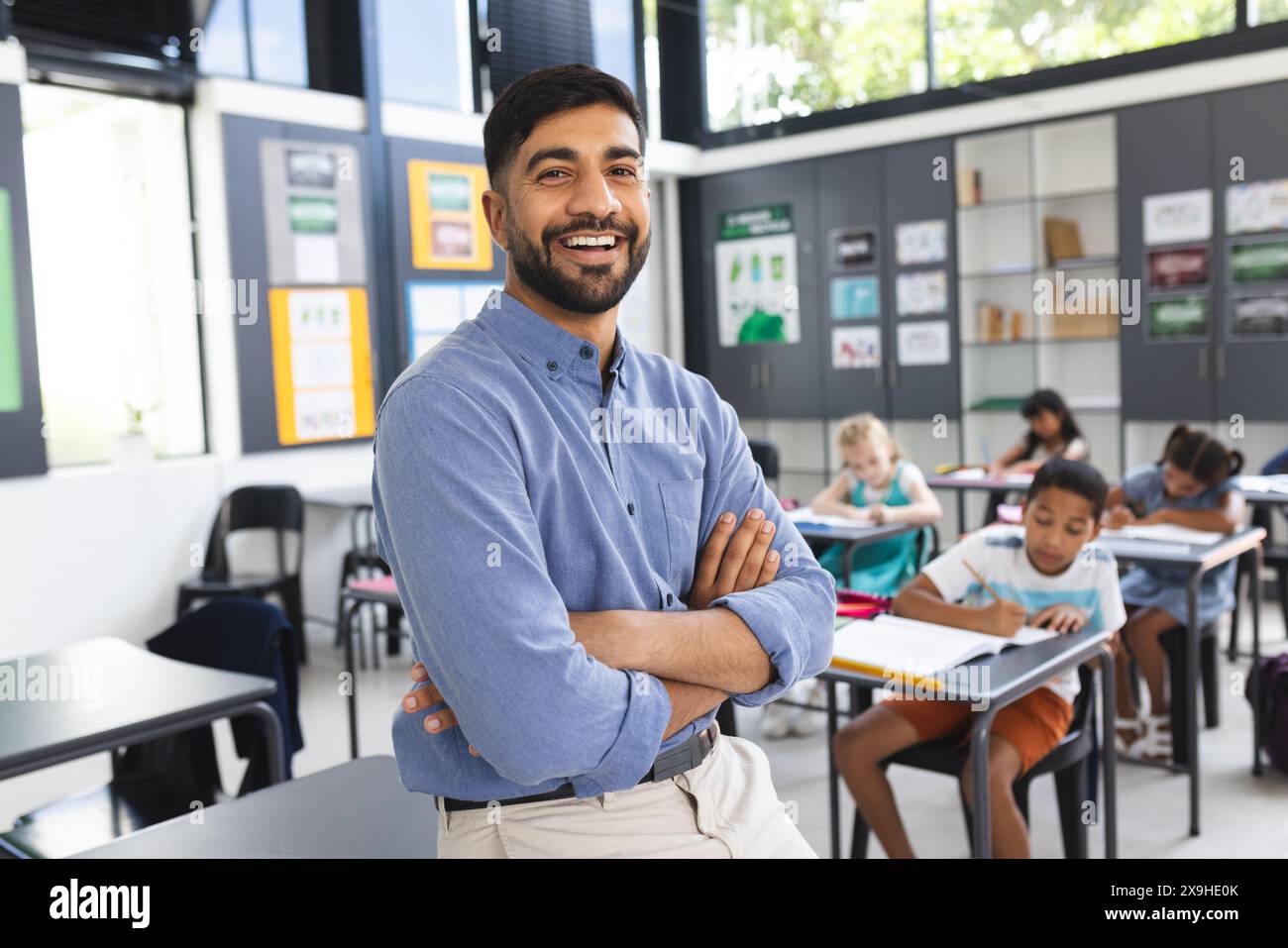 À l'école, un enseignant asiatique se tient souriant avec les bras croisés dans la salle de classe Banque D'Images