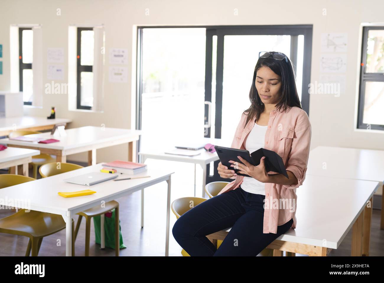 Une jeune enseignante biraciale utilise une tablette dans une salle de classe lumineuse au lycée Banque D'Images