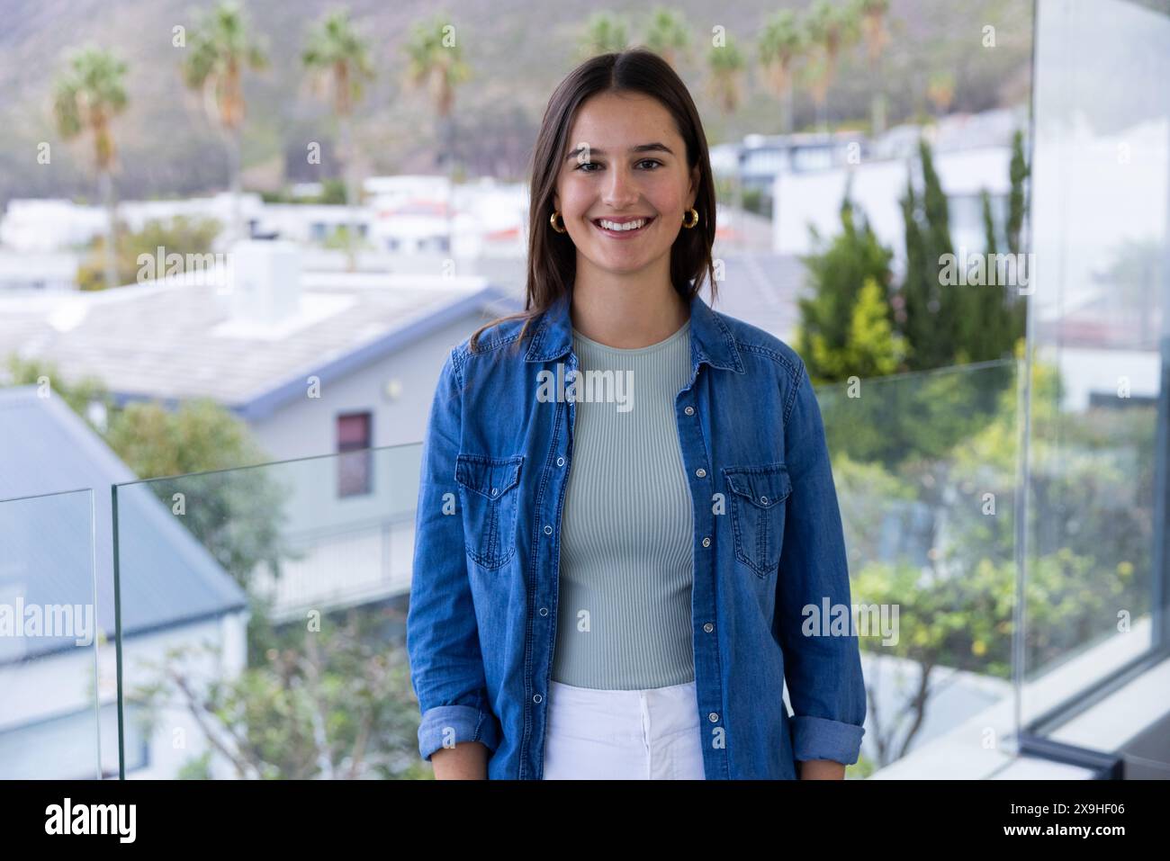 À la maison, jeune femme caucasienne souriante tout en se tenant debout sur le balcon dans un quartier résidentiel Banque D'Images