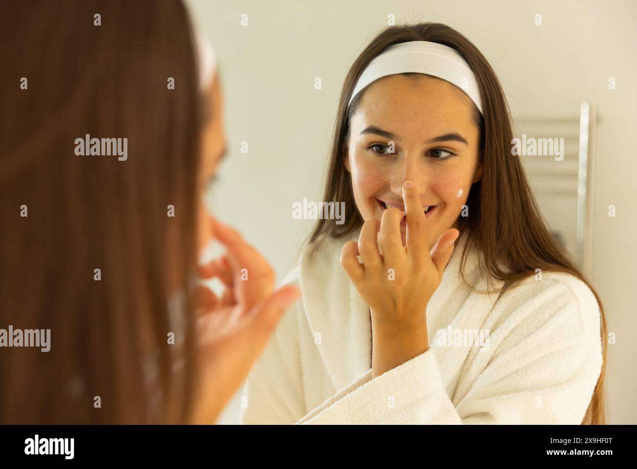 Jeune femme caucasienne applique des soins de la peau et sourit à son reflet à la maison Banque D'Images