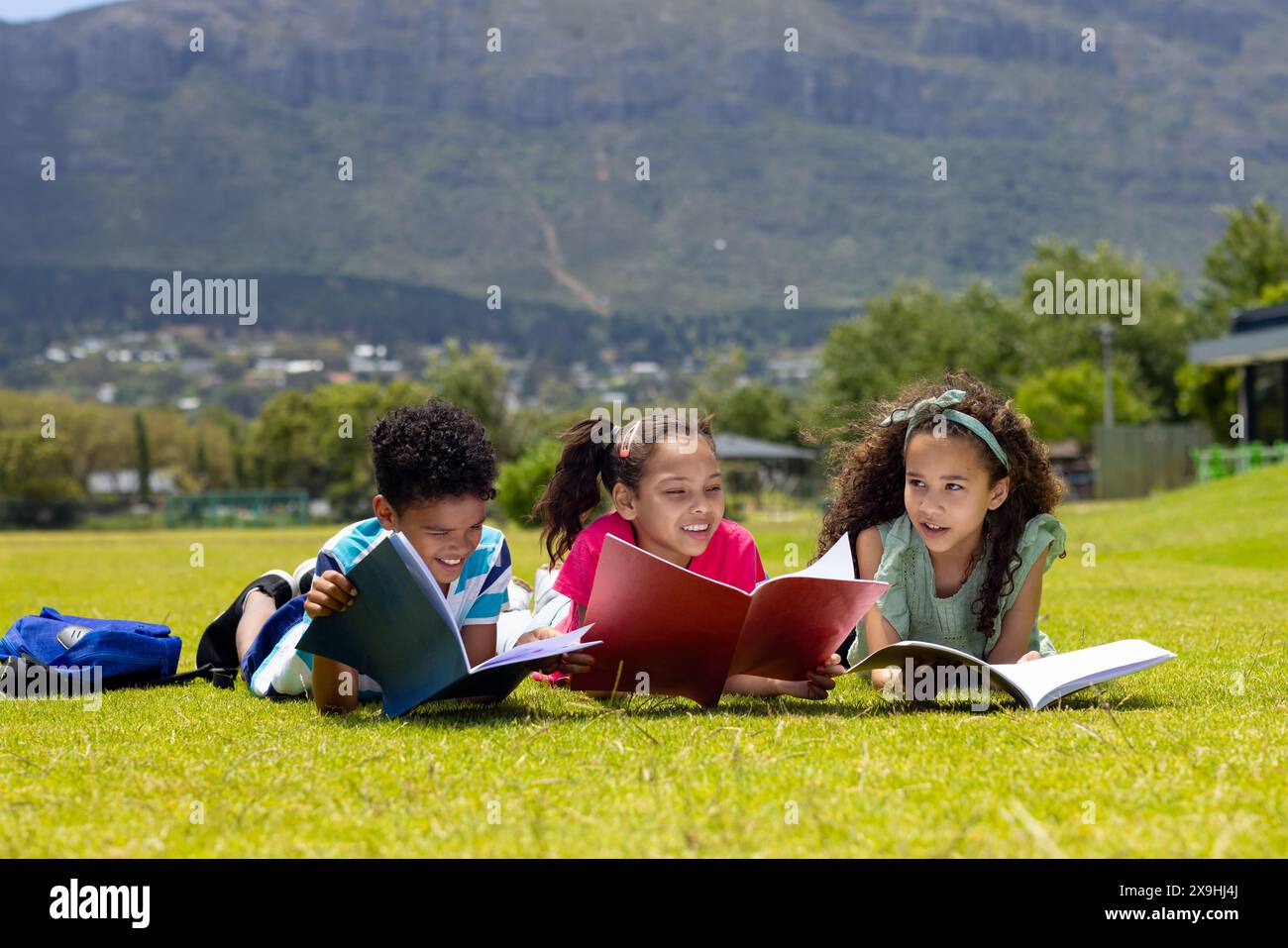 Biracial garçon et filles lisent des livres sur un champ d'herbe ensoleillé Banque D'Images